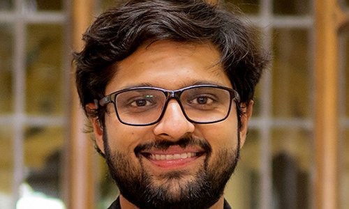 An image showing PhD student Dhruv Jain. He is wearing glasses and in a gray sports coat with a gray sweater and white shirt underneath