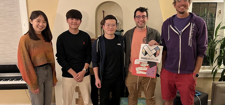 A picture of Chu, Jae, Xia, Daniel, and Jon standing in Jon's living room with Daniel holding a Makeability Lab sign