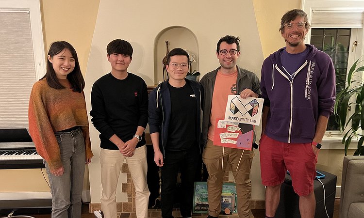 A picture of Chu, Jae, Xia, Daniel, and Jon standing in Jon's living room with Daniel holding a Makeability Lab sign