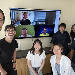 A picture of the Makeability Lab standing in front of a large-screen TV showing remote Zoom ML members and Josh