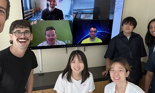 A picture of the Makeability Lab standing in front of a large-screen TV showing remote Zoom ML members and Josh