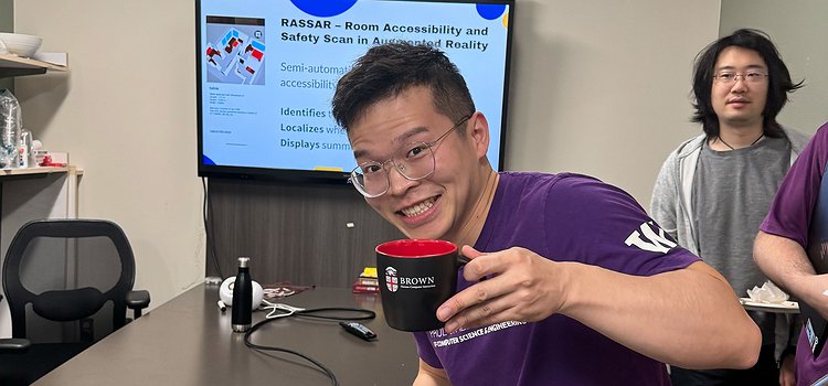 Xia Su holding up a Brown University mug with his talk slides in the background