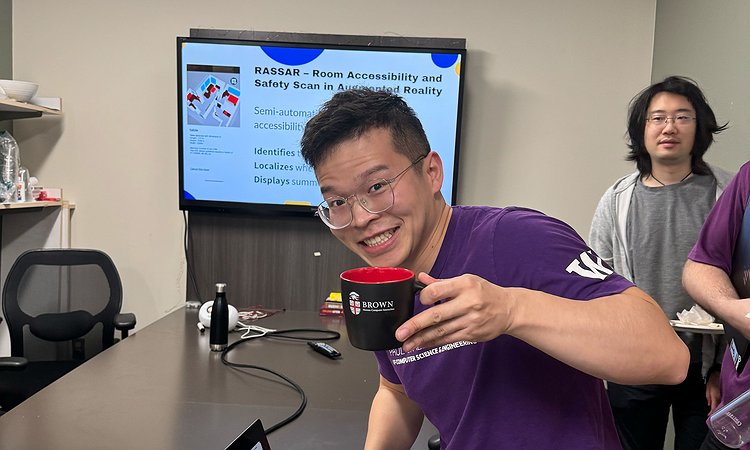 Xia Su holding up a Brown University mug with his talk slides in the background