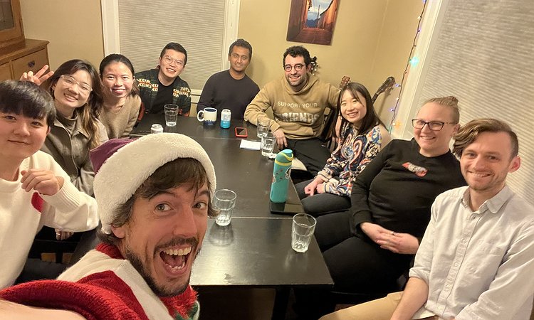 An image of Makeability Lab seated around a table including Jon with a Santa hat on and some guitars in the background