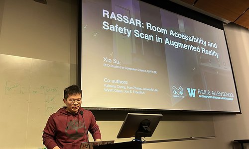 Xia Su standing in front of his title slide stating "RASSAR: Room Accessibility and Safety Scan in Augmented Reality"
