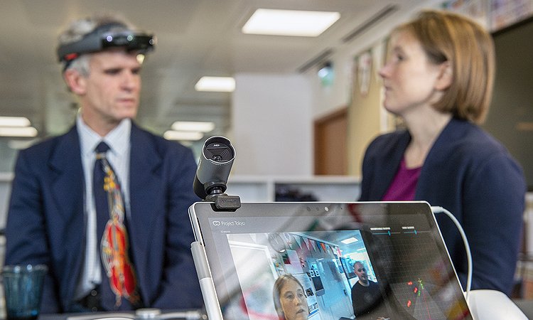 Project Tokyo uses an adapted HoloLens and real-time computer vision to recognize people's faces. This image shows a blind person wearing the HoloLens (augmented reality head-mounted display) and looking at a nearby person's face.