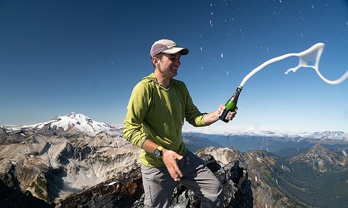 Galen Weld on top of Buck Mountain, the final climb out of the 100 highest mountains in Washington. Galen is holding a champagne bottle spraying champagne!