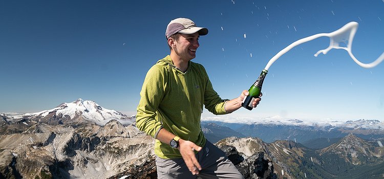 Galen Weld on top of Buck Mountain, the final climb out of the 100 highest mountains in Washington. Galen is holding a champagne bottle spraying champagne!