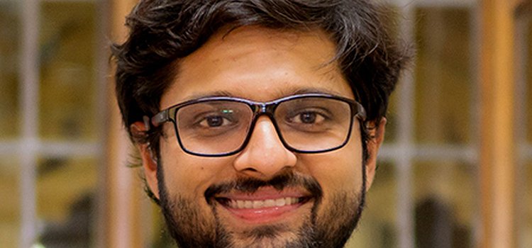 An image showing PhD student Dhruv Jain. He is wearing glasses and in a gray sports coat with a gray sweater and white shirt underneath
