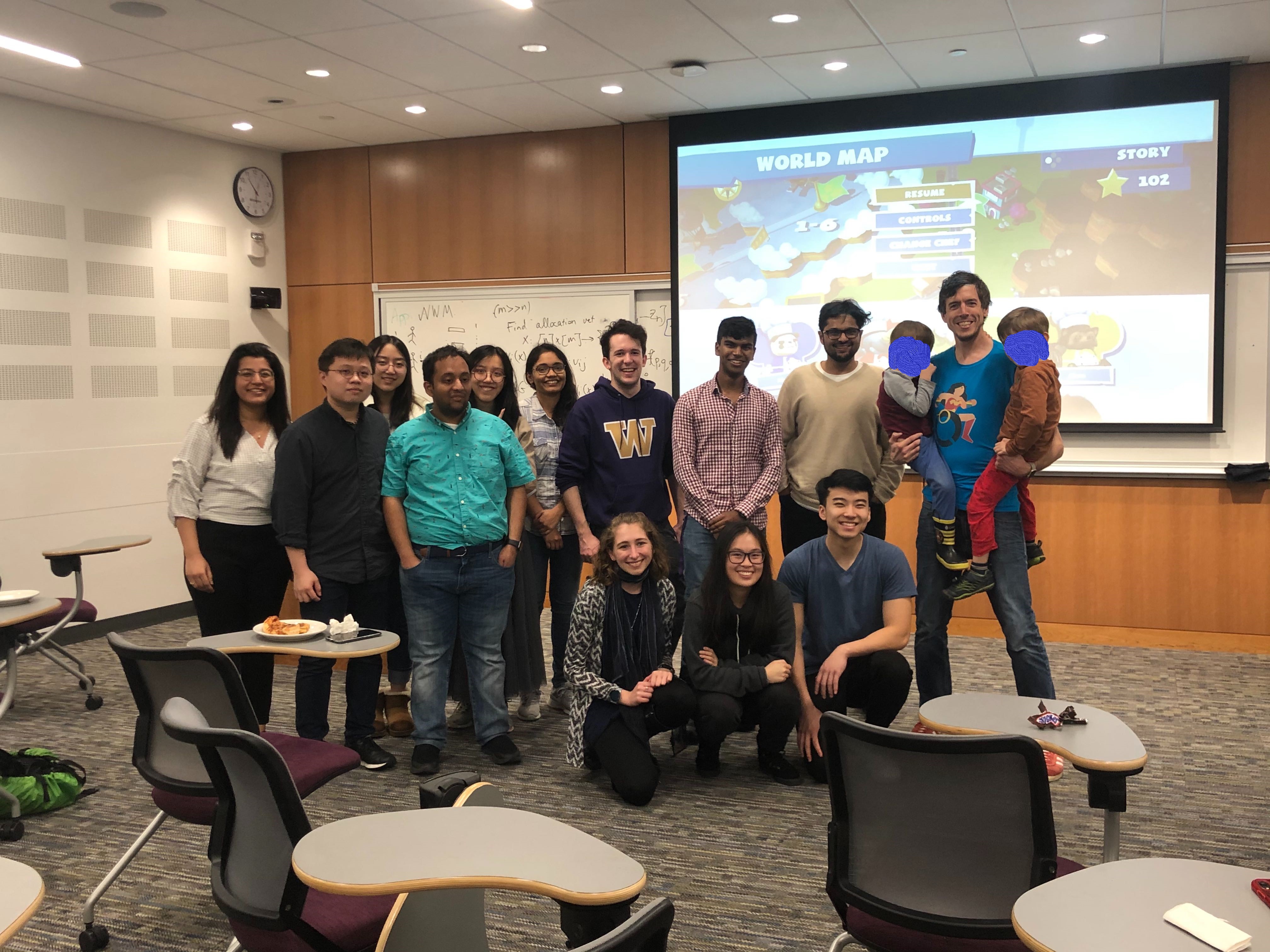 A picture from the Makeability Lab game night showing two rows of people (ugrad, MS, and PhD members of the lab) with the Overcooked Switch game in the background (projected on a screen)
