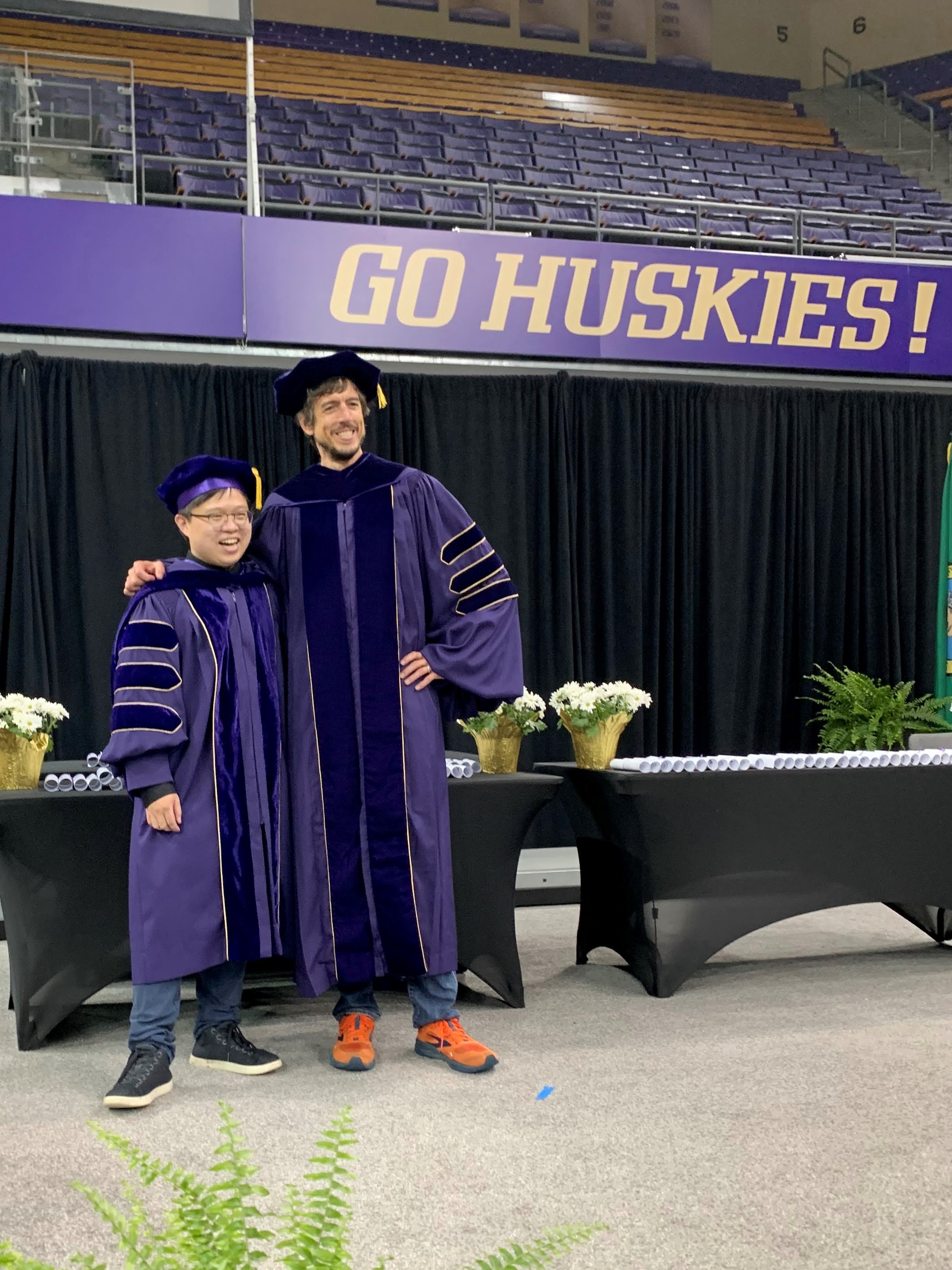 Jon and Liang standing together with a "Go Huskies" sign in the background
