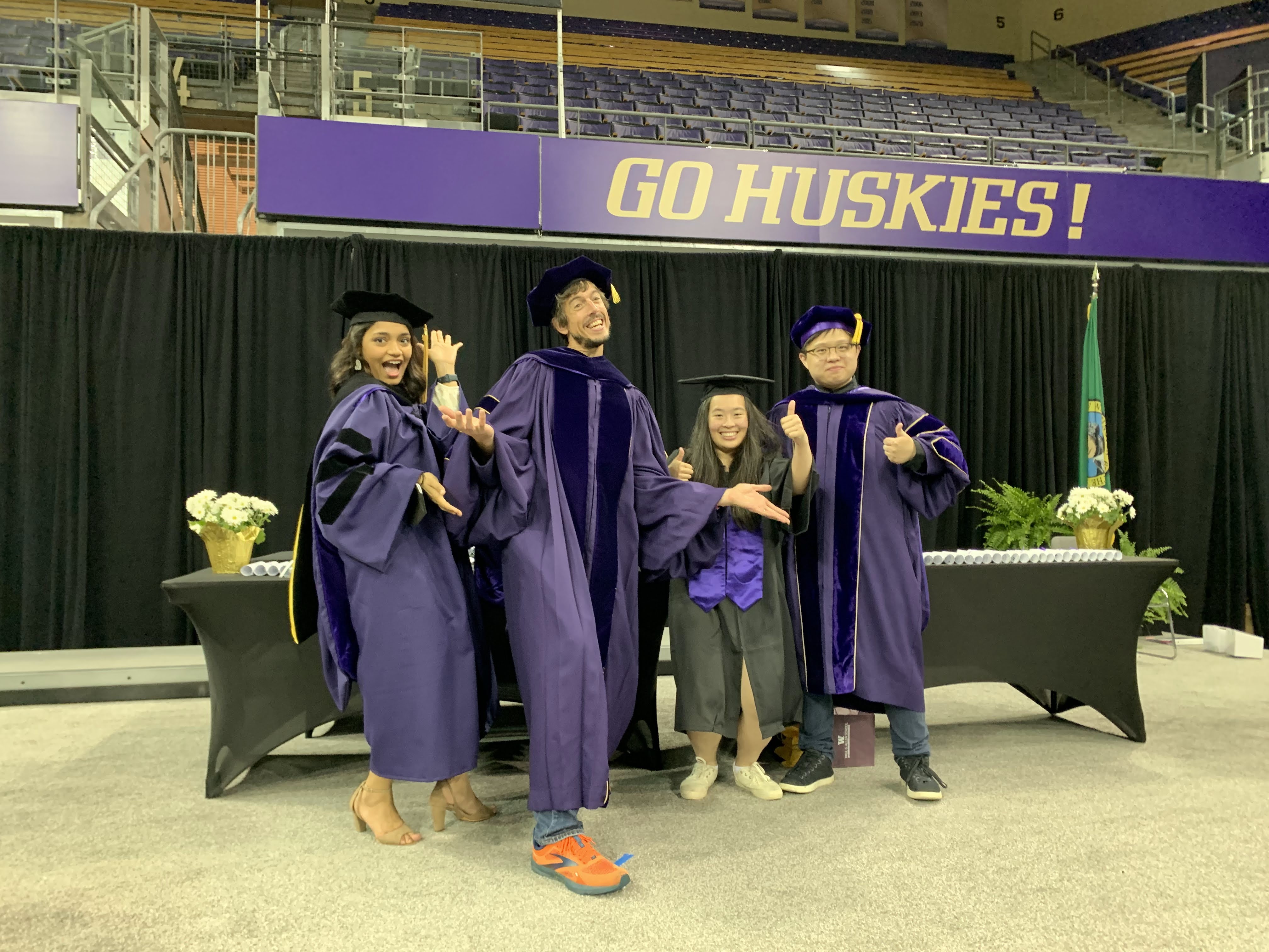 Manaswi, Jon, Aileen, and Liang standing in their graduation gowns with silly expressions